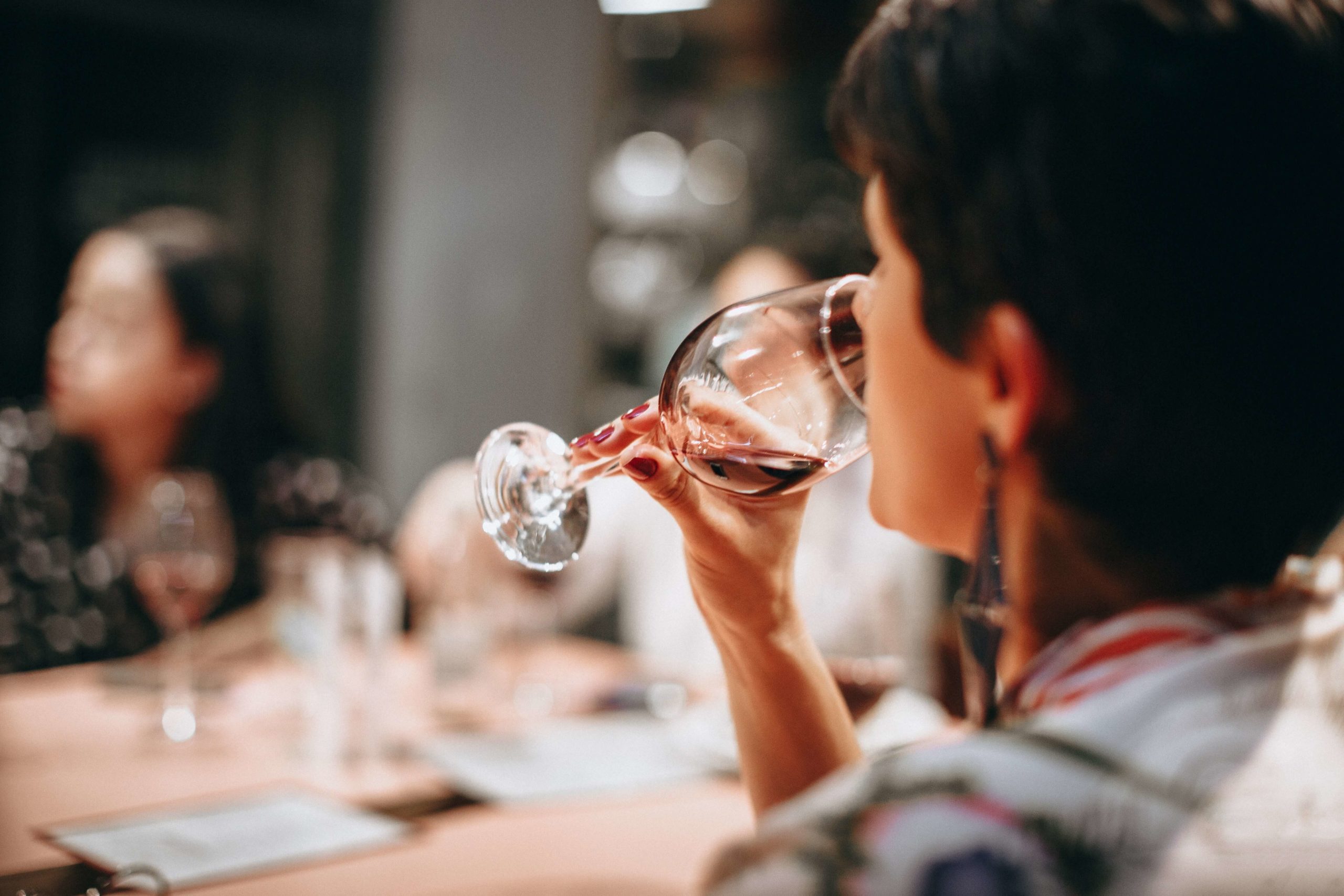 Mujer catando un vino tinto en una mesa con más personas